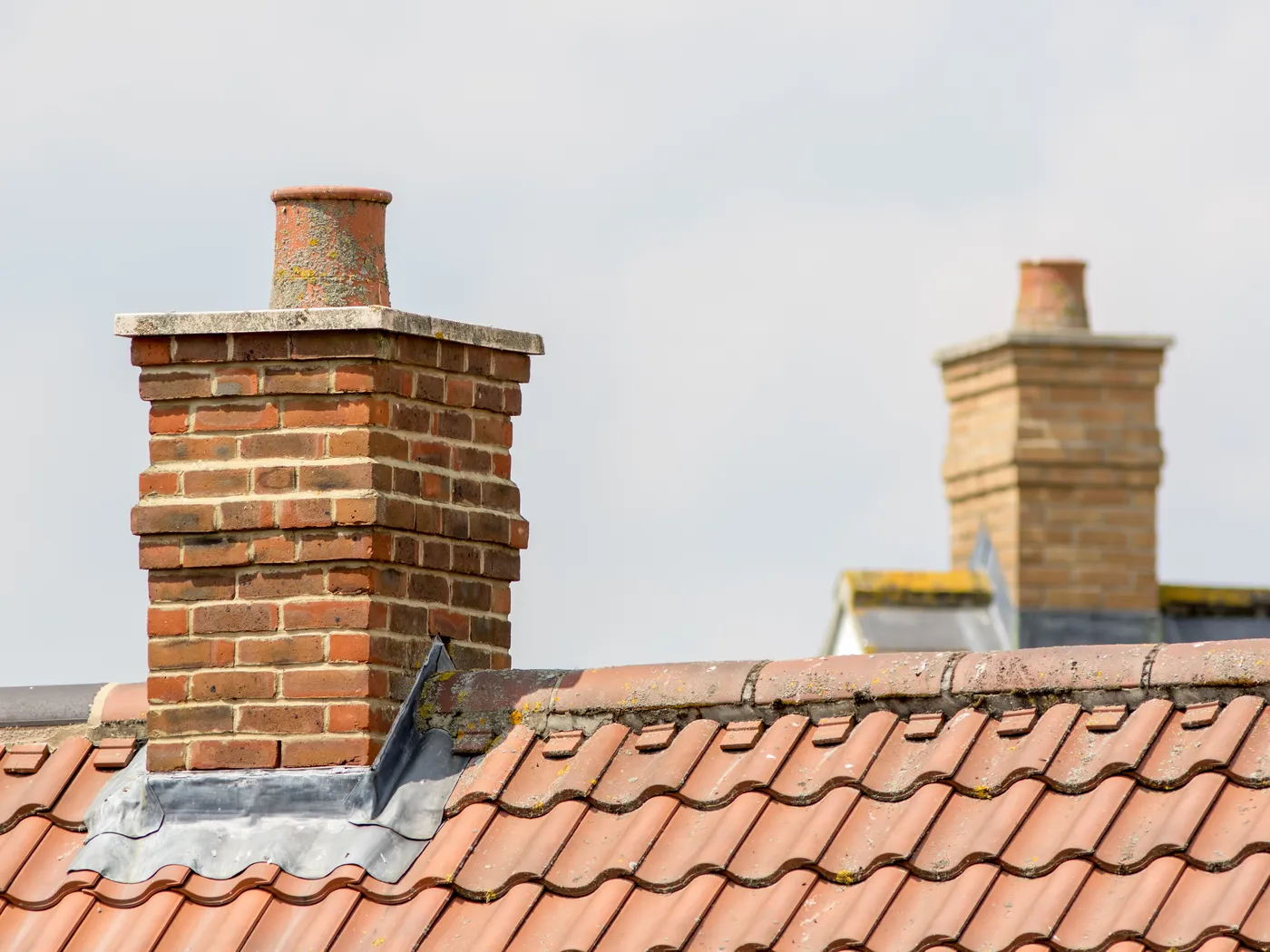 A brick chimney stack with lead flashing on a tiled roof